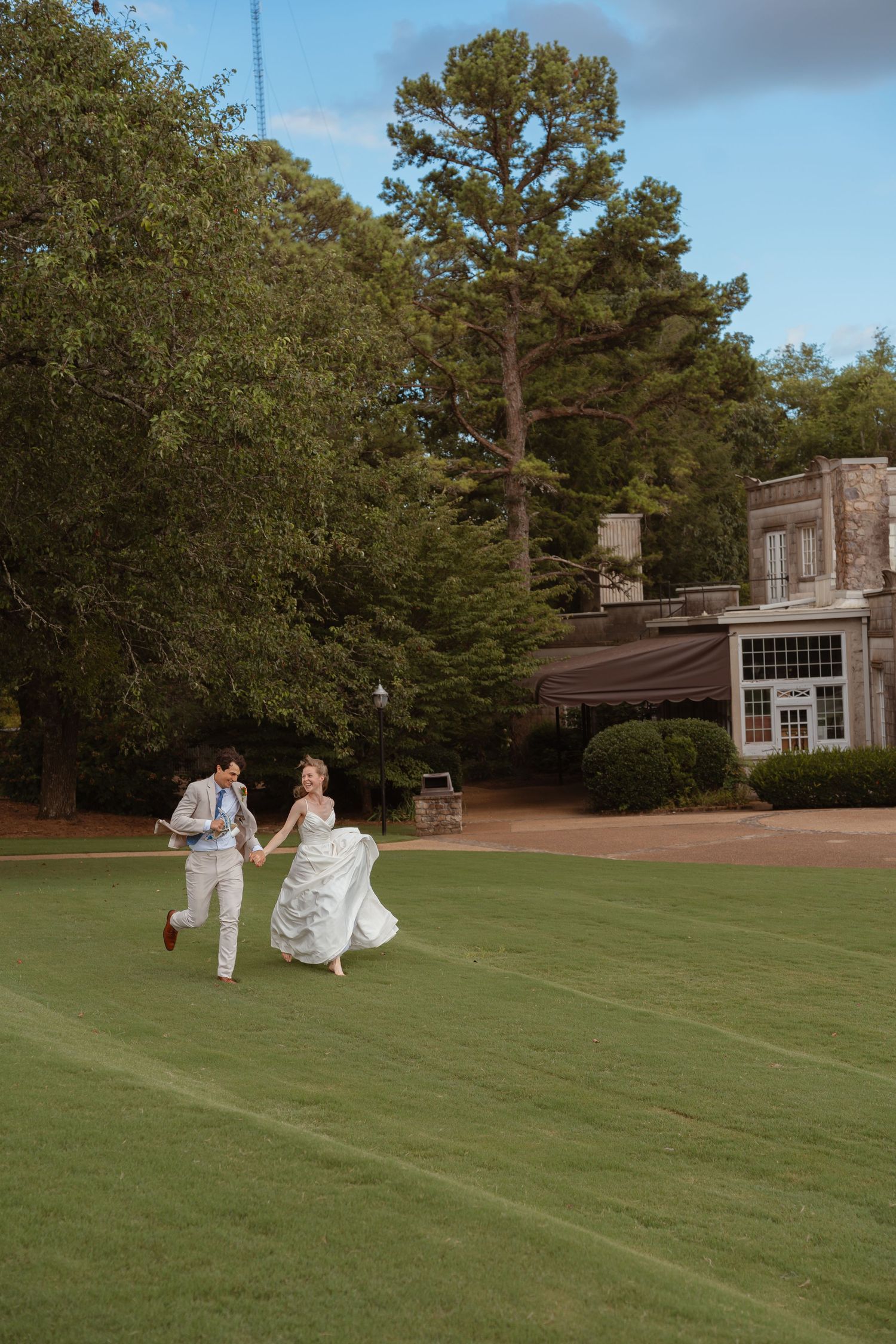 Romantic couple in formal wear embracing near blooming white roses by a lakeside path.