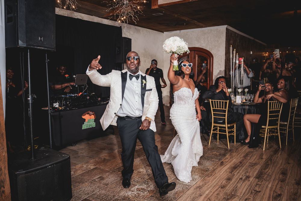 Bride and groom make grand entrance at wedding reception, bride holding bouquet, both wearing masks, guests seated at gold chairs.