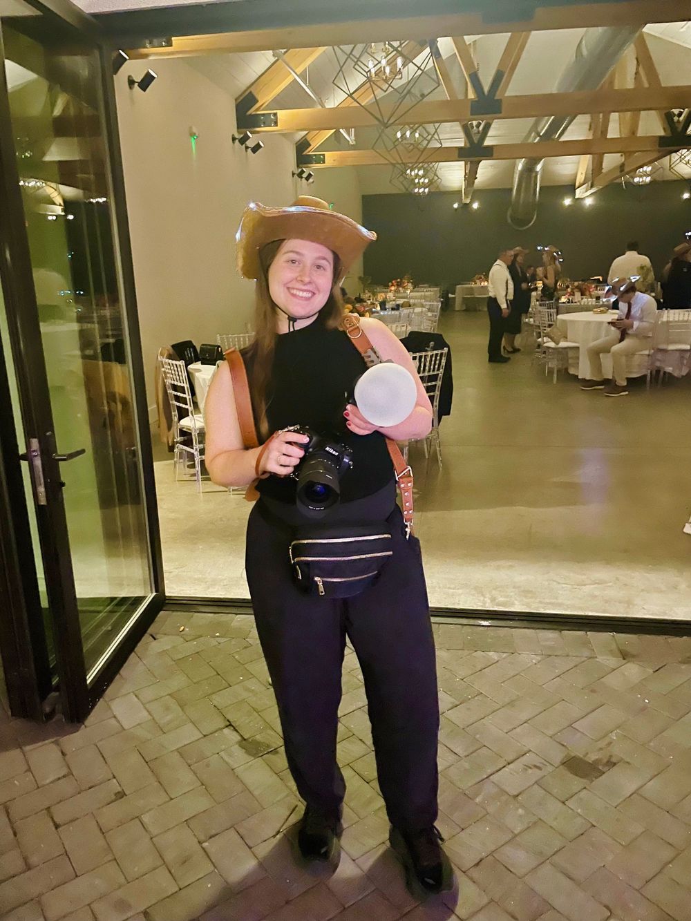Event photographer in black attire carrying camera equipment at a reception venue.