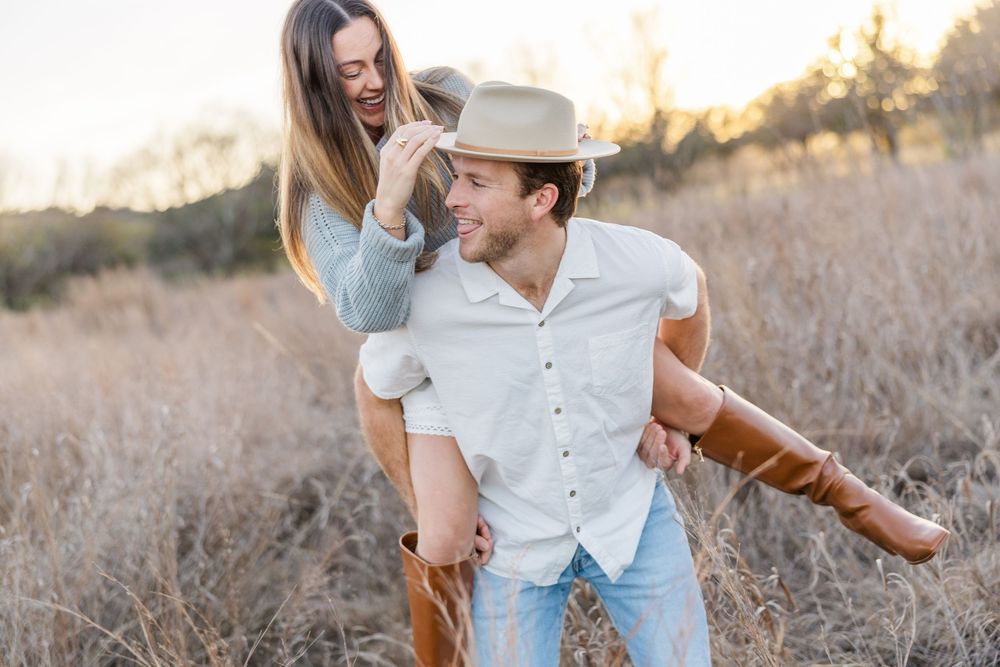 A playful couple shares a joyful moment in a sunlit field with tall grass during golden hour.
