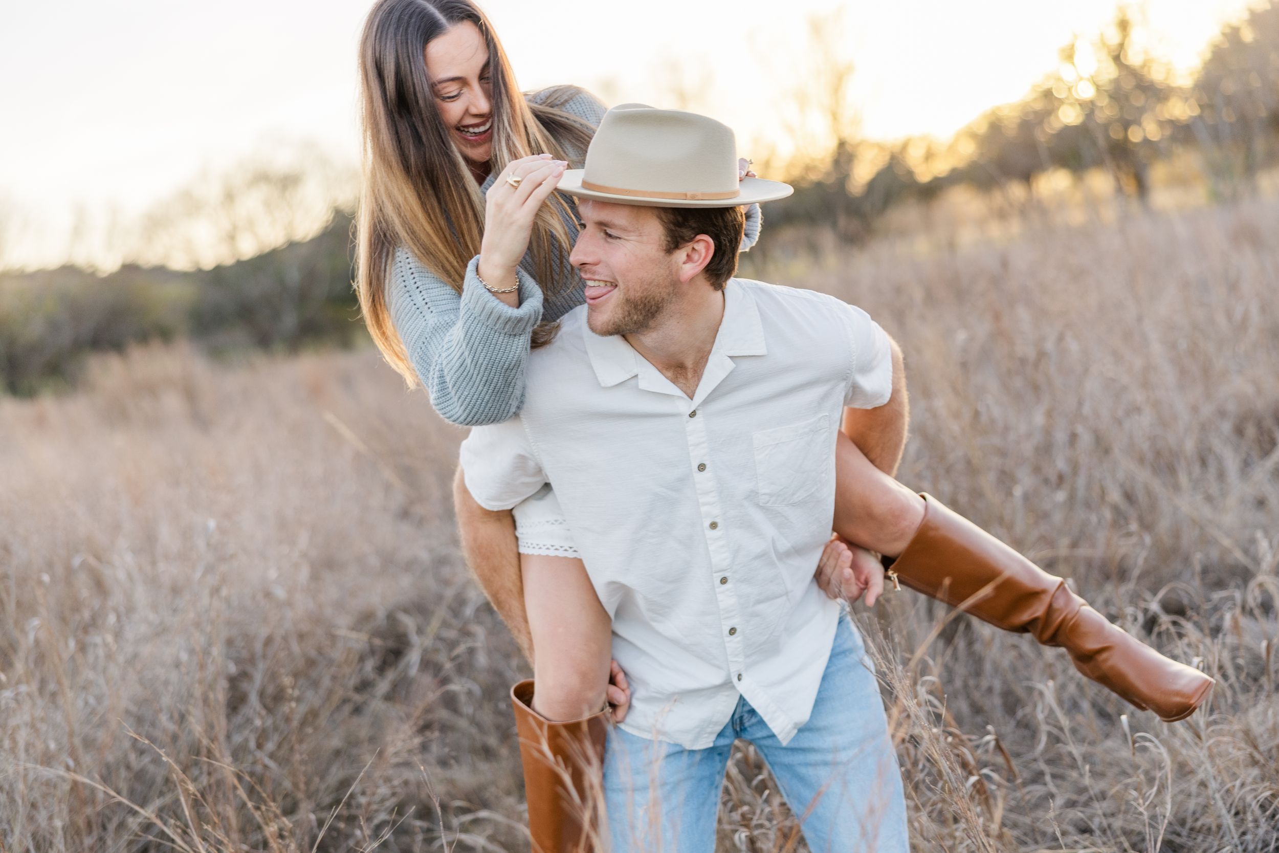 A playful couple shares a joyful moment in a sunlit field with tall grass during golden hour.