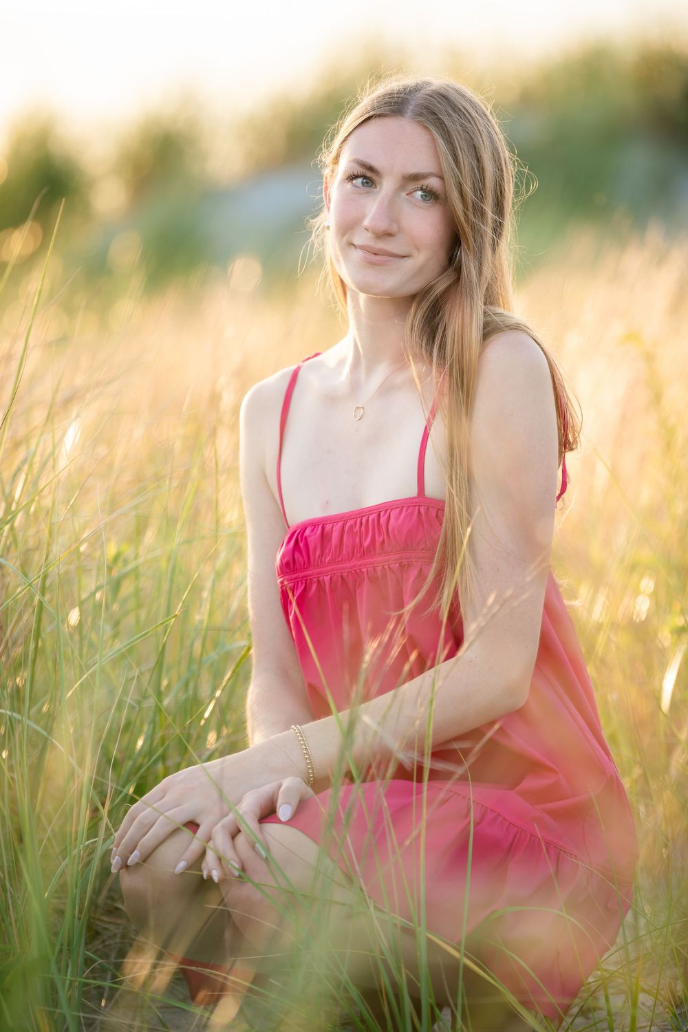 Young woman in pink sundress sitting in tall golden grass field during sunset golden hour.