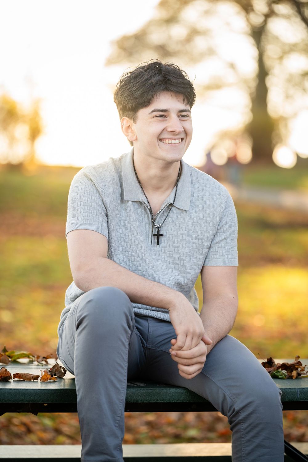 Person sitting on wooden bench outdoors during golden hour with autumn leaves scattered on ground.