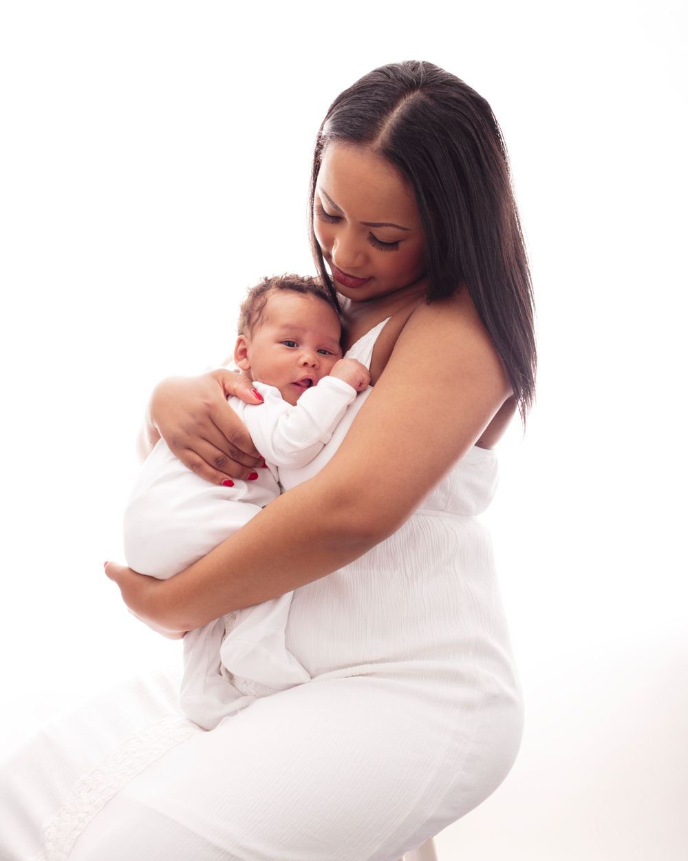 Tender moment between mother and newborn baby wrapped in white against bright background.
