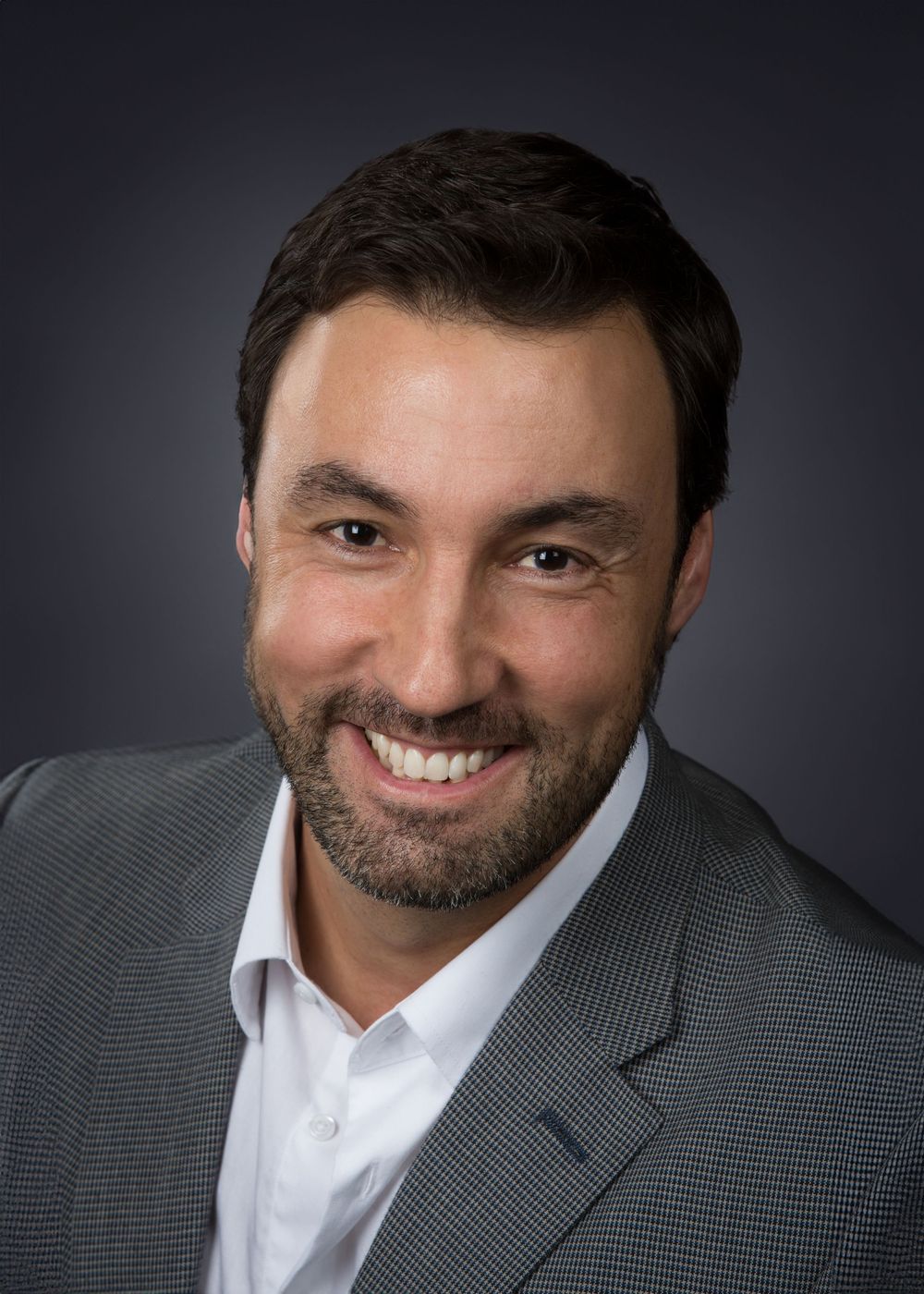 Professional headshot against dark background wearing grey suit jacket.
