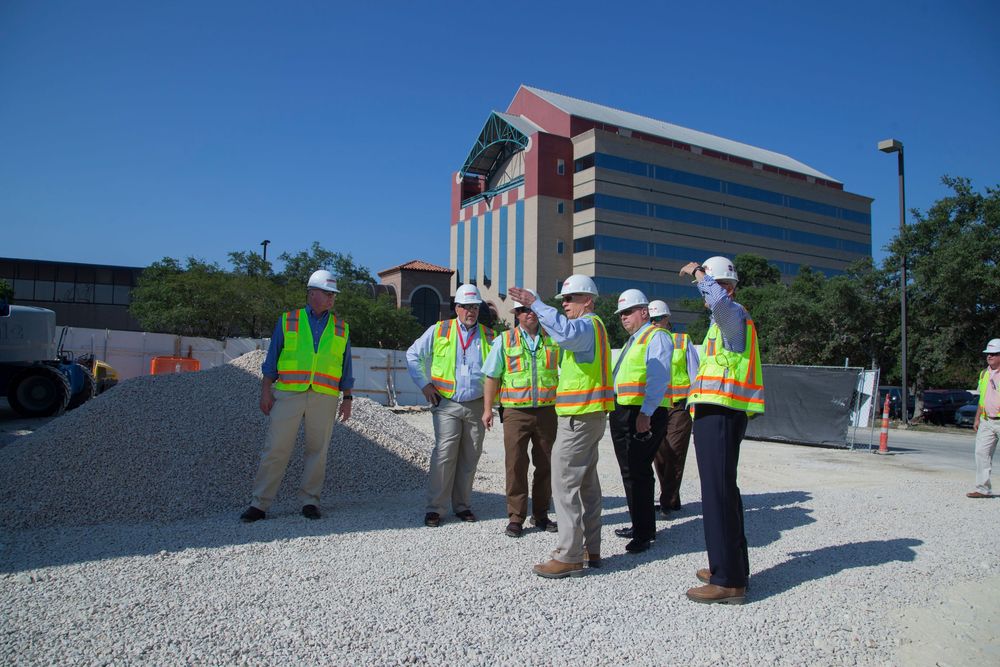 Construction workers in safety vests inspect a commercial building rooftop on a sunny day.