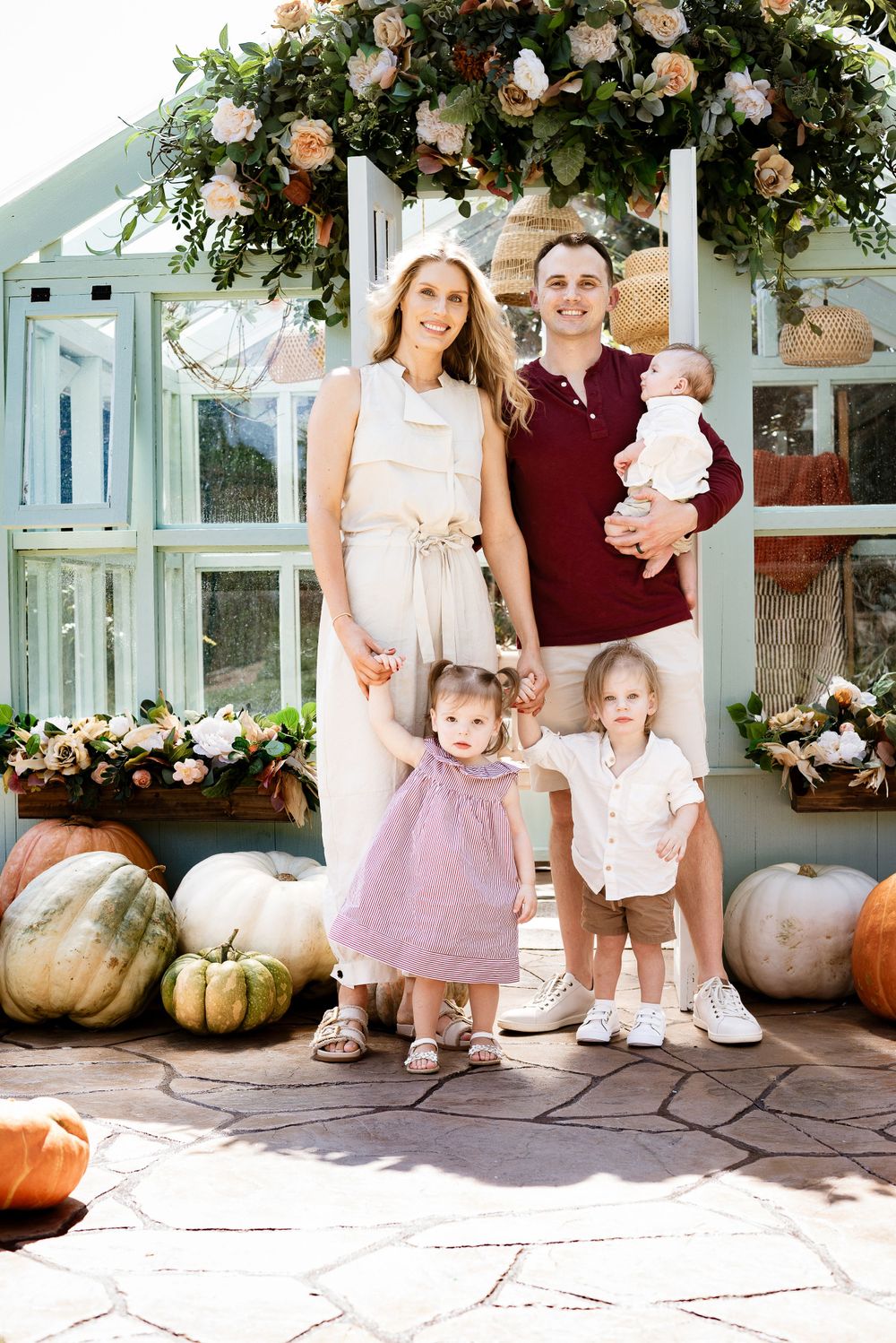 A family gathering on a stone patio with floral arch and seasonal pumpkin decorations.
