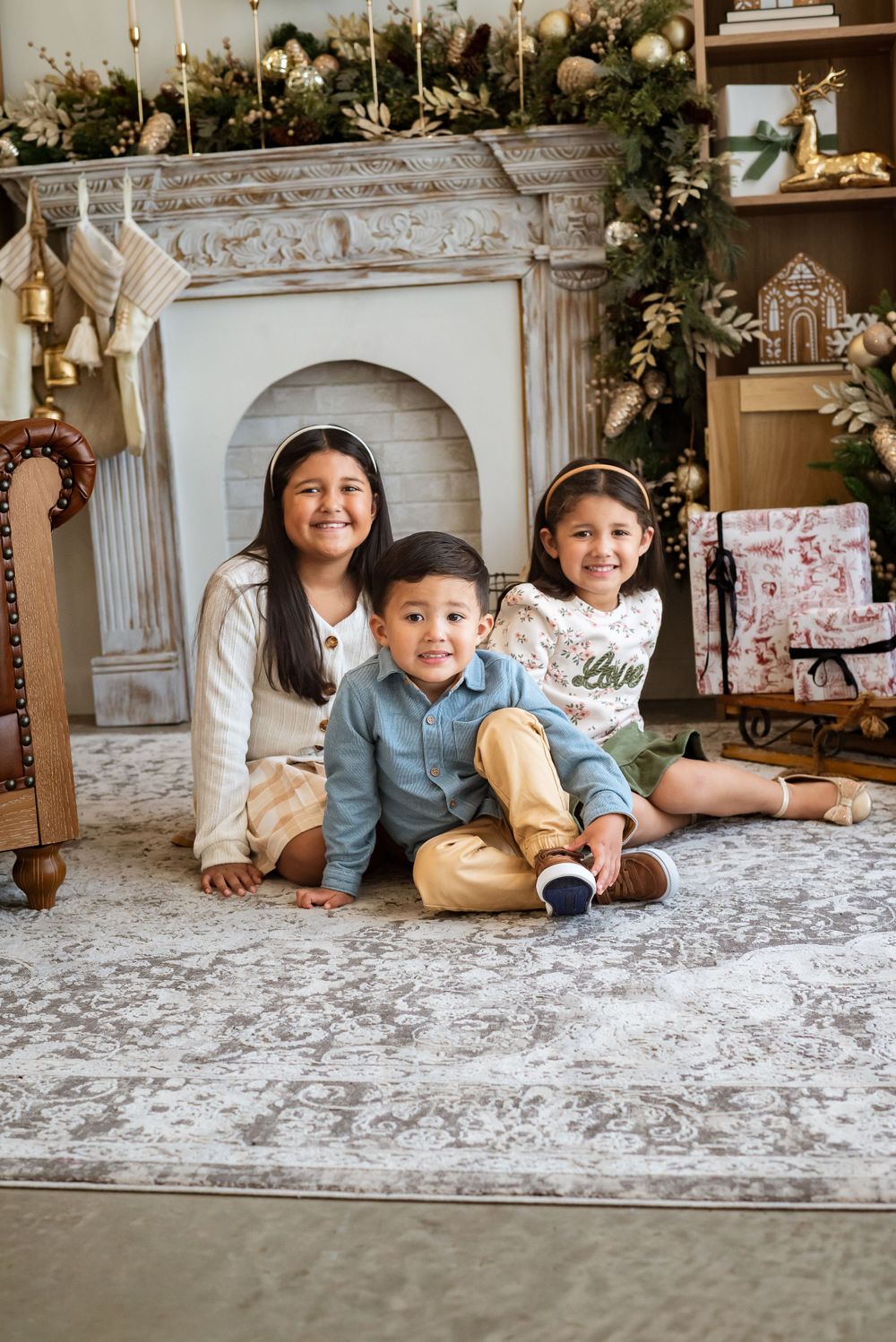 Children sitting on floor in front of decorated holiday fireplace and mantle.