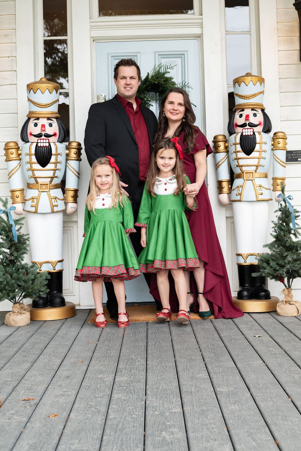 Holiday portrait on porch with large nutcracker decorations and matching green dresses.