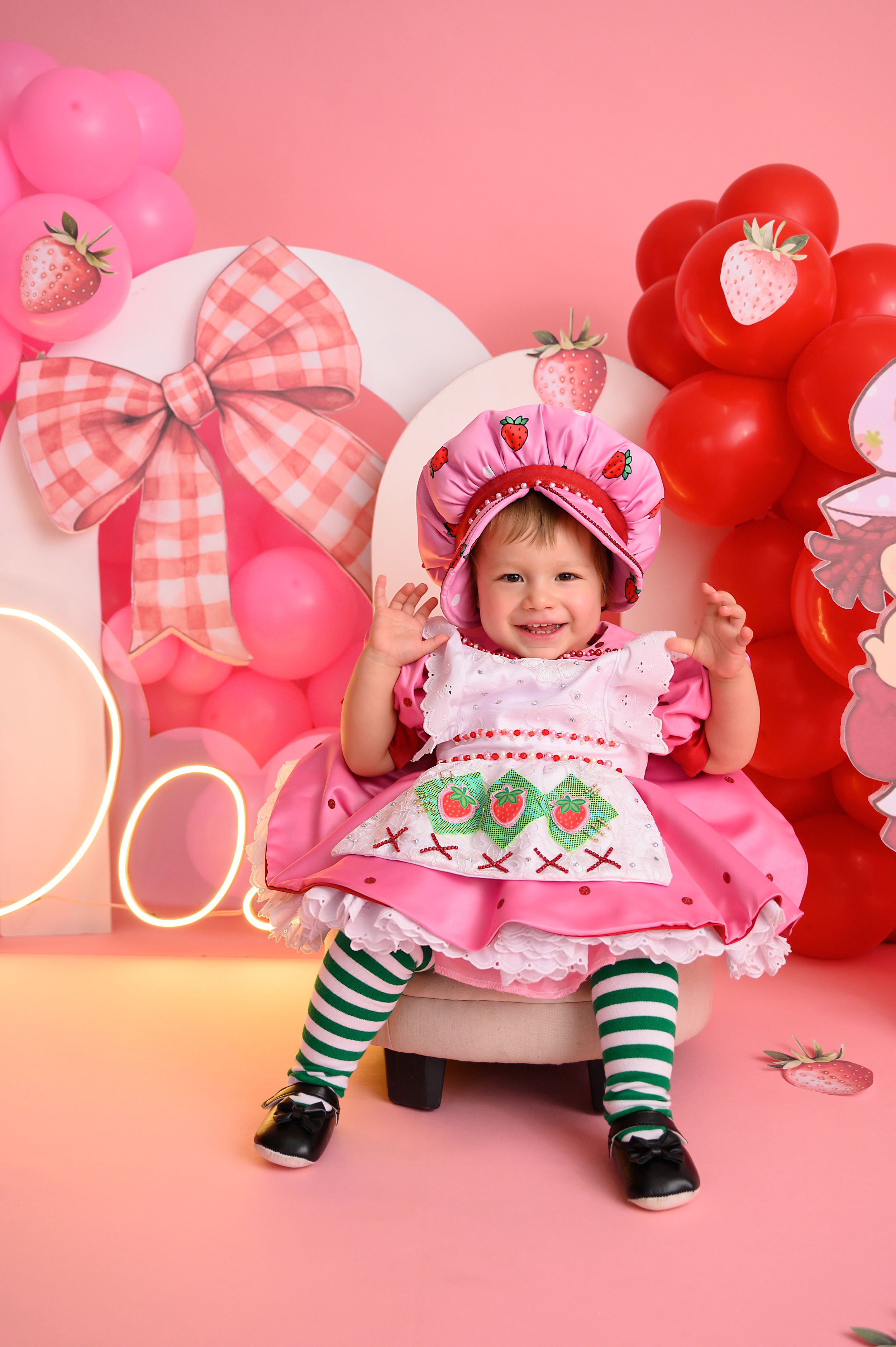 Whimsical strawberry-themed photo setup with pink dress, striped socks and balloons.