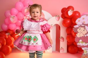 Festive pink and red balloon display with strawberry decorations against pink wall.