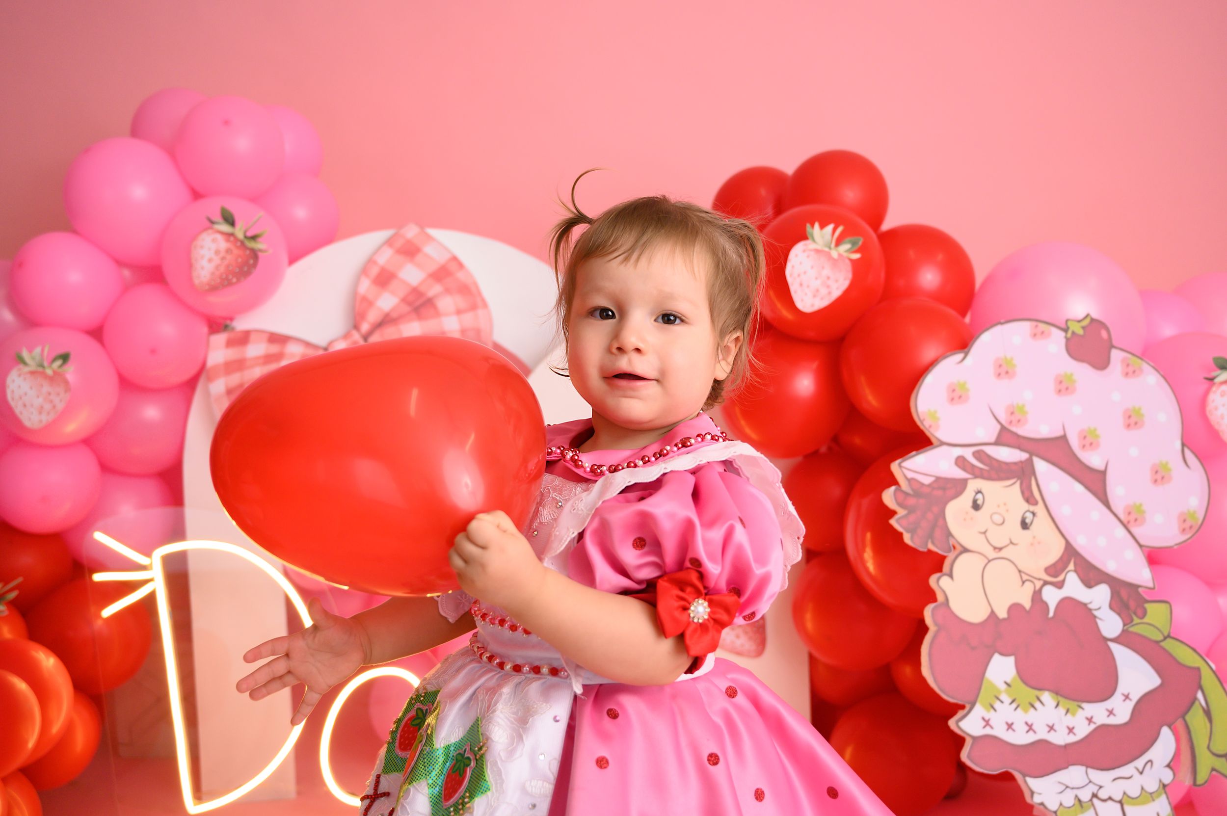 Pink and red balloon decorations with strawberry theme against pink background.