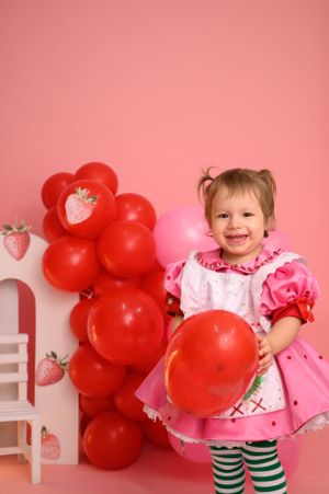 Festive strawberry-themed setup with red and pink balloons against pink wall.