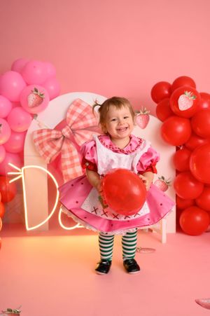 Playful scene with pink dress, balloons and strawberry decorations on pink background.