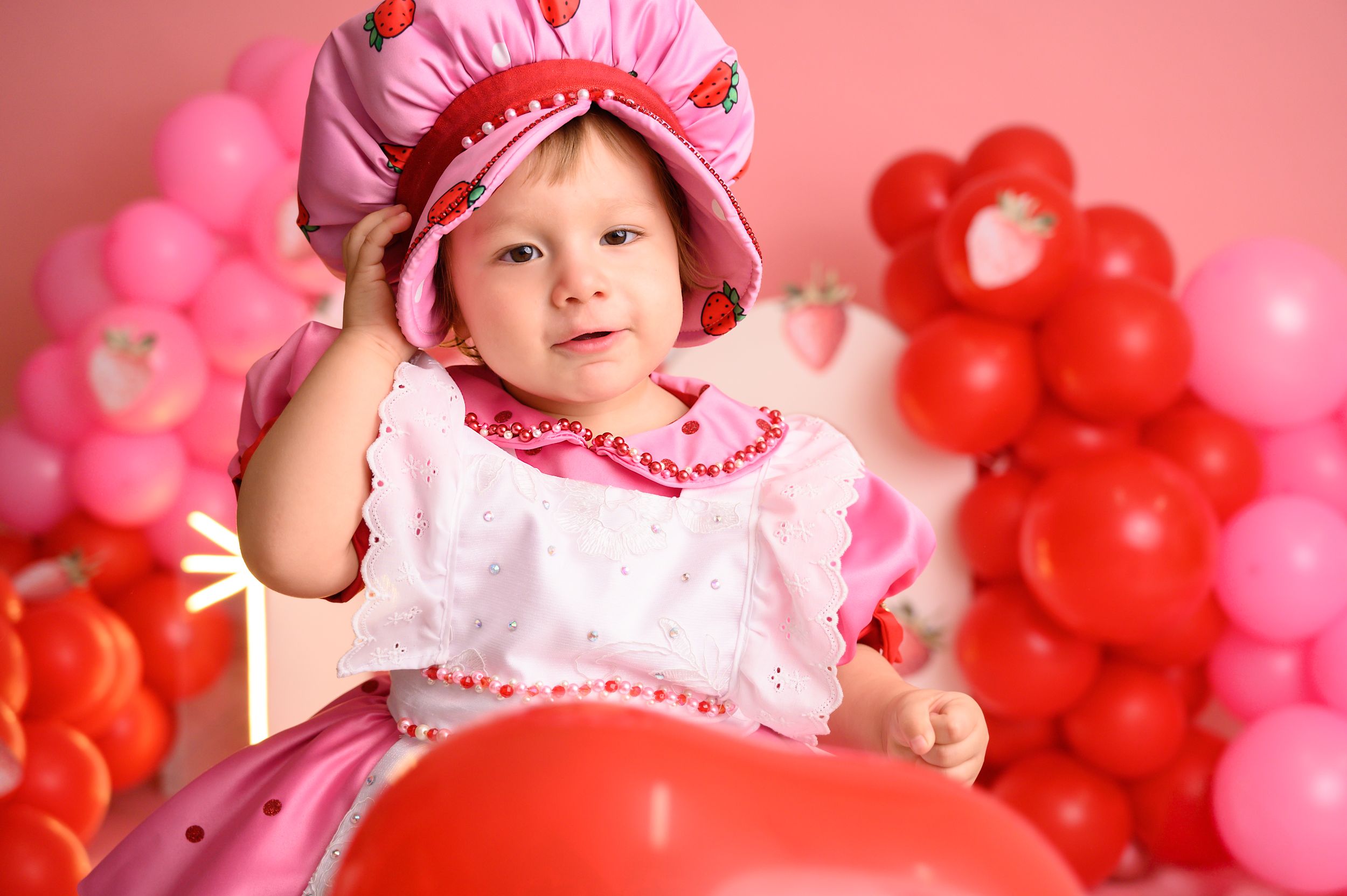 Pink party setup with strawberry theme and balloon decorations.