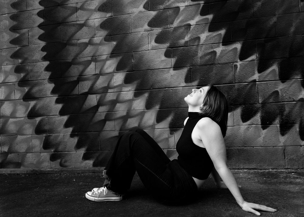 Dramatic black and white photo of person resting against geometric wall.