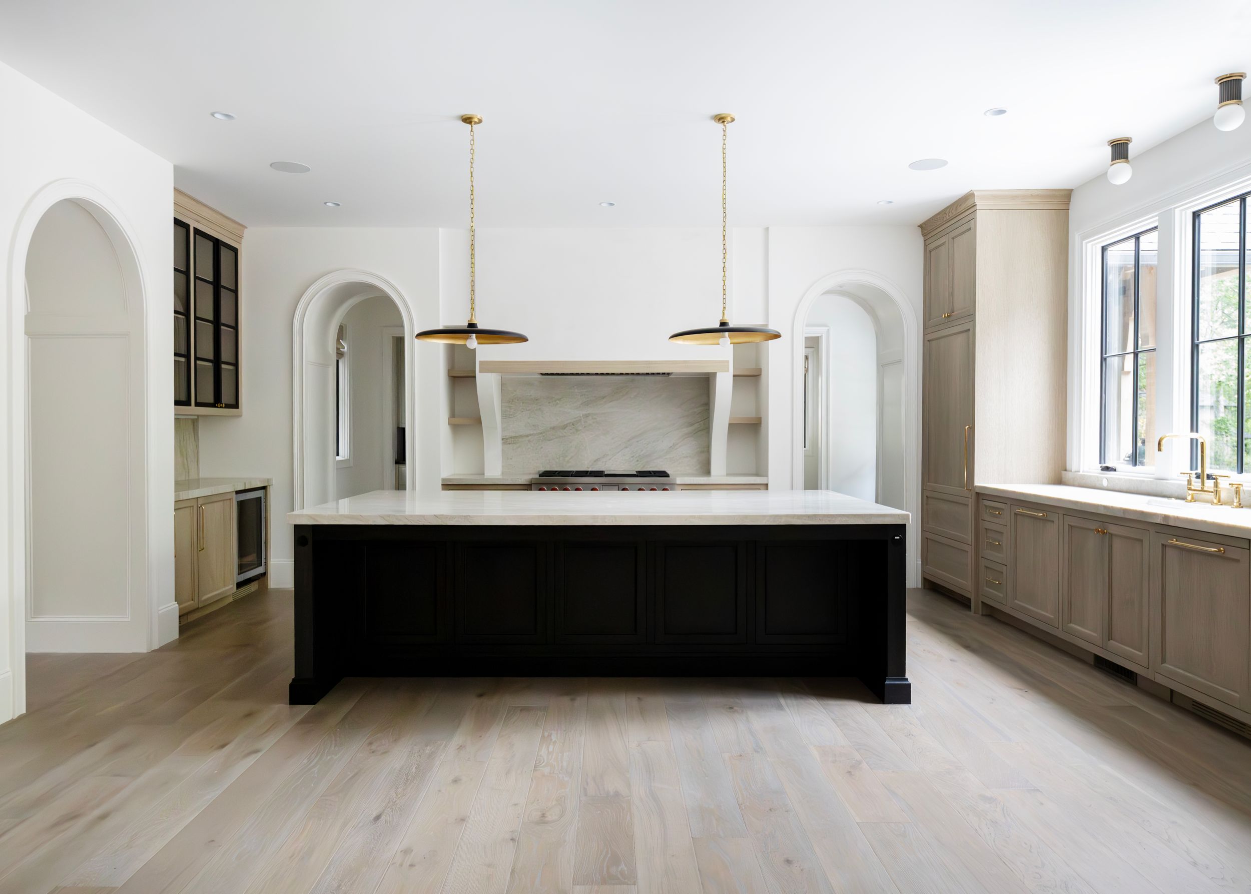 Modern kitchen with arched doorways, black island, and light wood floors.