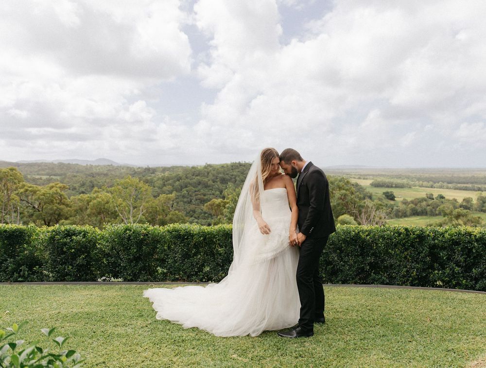 Bride and groom sharing intimate moment in garden with stunning countryside panoramic views behind them.