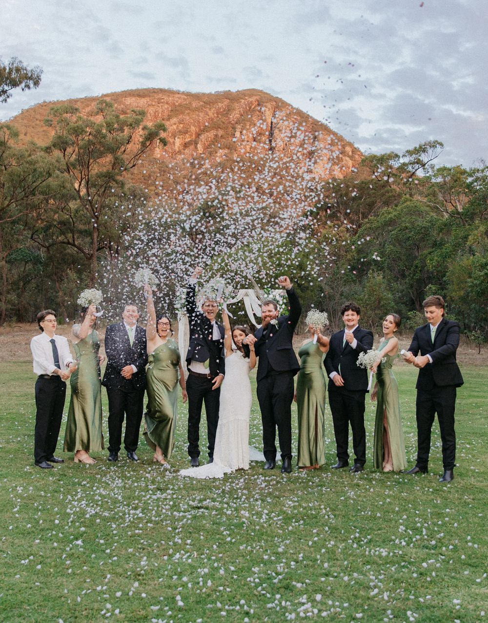 Wedding party celebrating with confetti in front of a stunning red mountain backdrop in Australia.