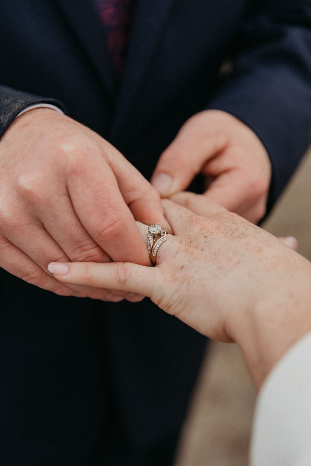 Groom placing diamond engagement ring onto bride's hand during wedding ceremony close-up.