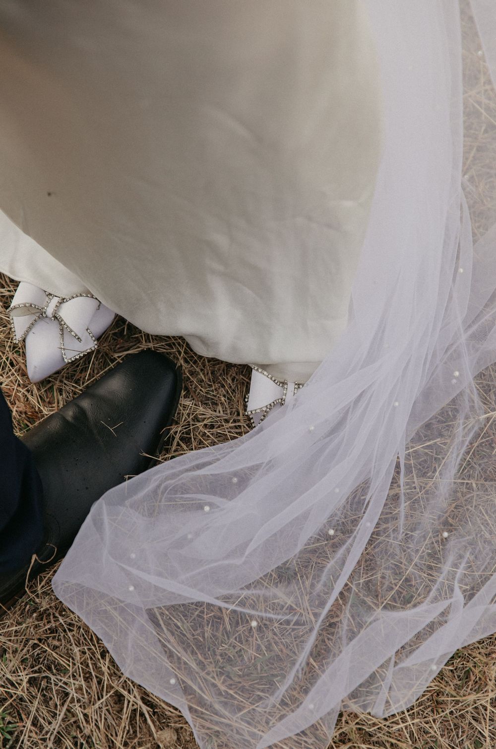 Close-up of bride's white embellished shoes and groom's black shoes with pearl-dotted veil.