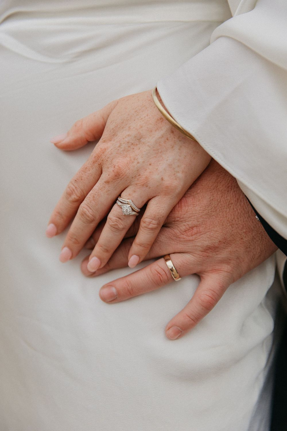 Close-up of newlywed couple's hands showing wedding rings, bride wearing diamond engagement ring and gold bracelet.