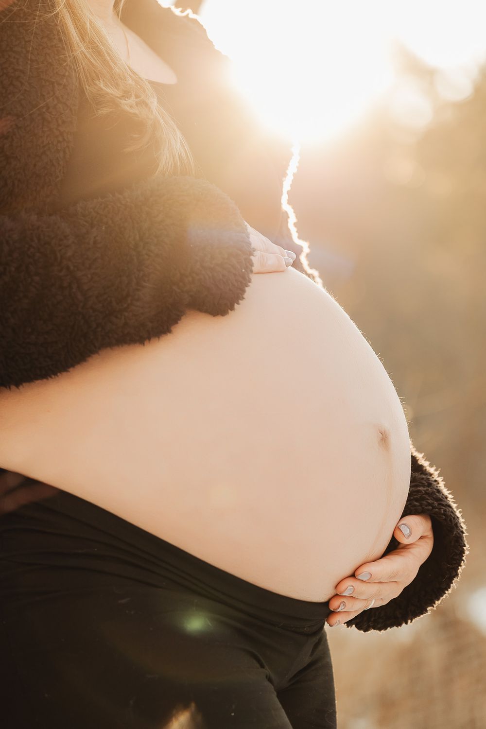 Close-up maternity photo showing pregnant belly silhouetted against golden sunlight in an outdoor setting.
