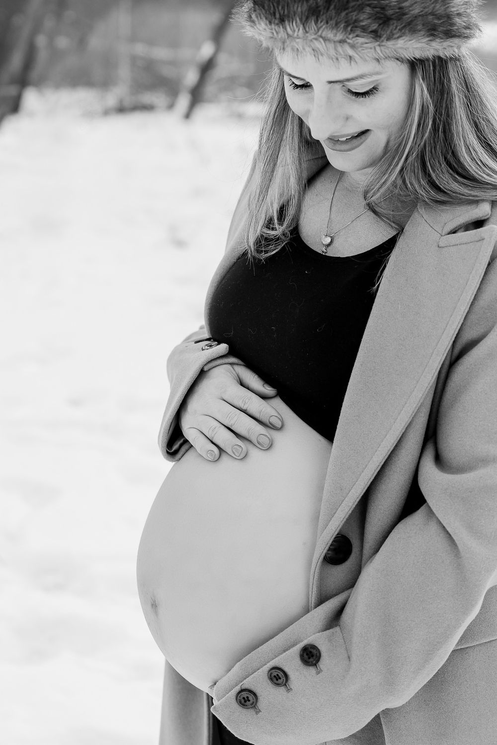 Black and white maternity portrait showing a tender moment with hands cradling baby bump in winter.