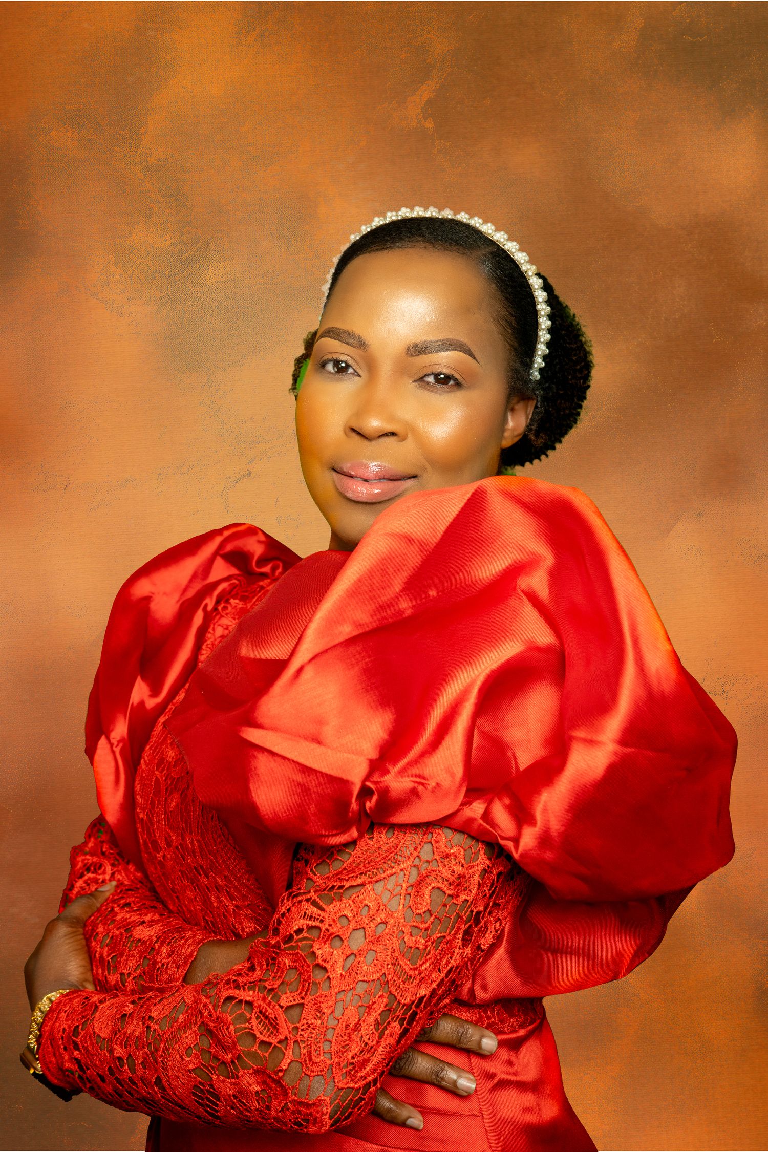 A woman in a vibrant red satin and lace dress with a pearl headband poses for a studio portrait.