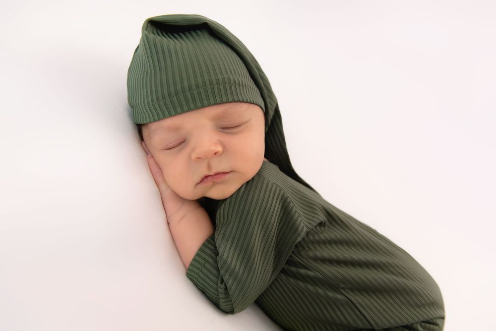 Sleeping baby wrapped in olive green knit fabric on white background.