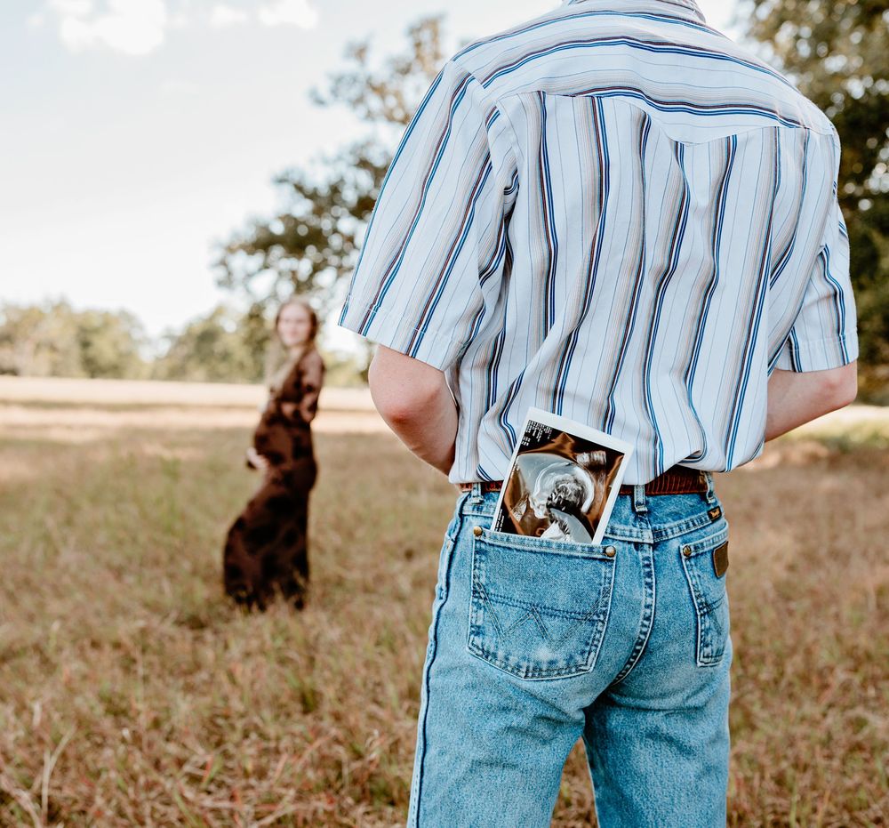 Man with ultrasound picture in pocket while his pregnant partner stand in a distance out of focus holding her belly in brazoria county texas
