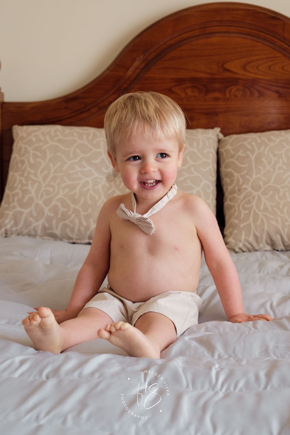 Bebe sentado na cama com laço de batizado