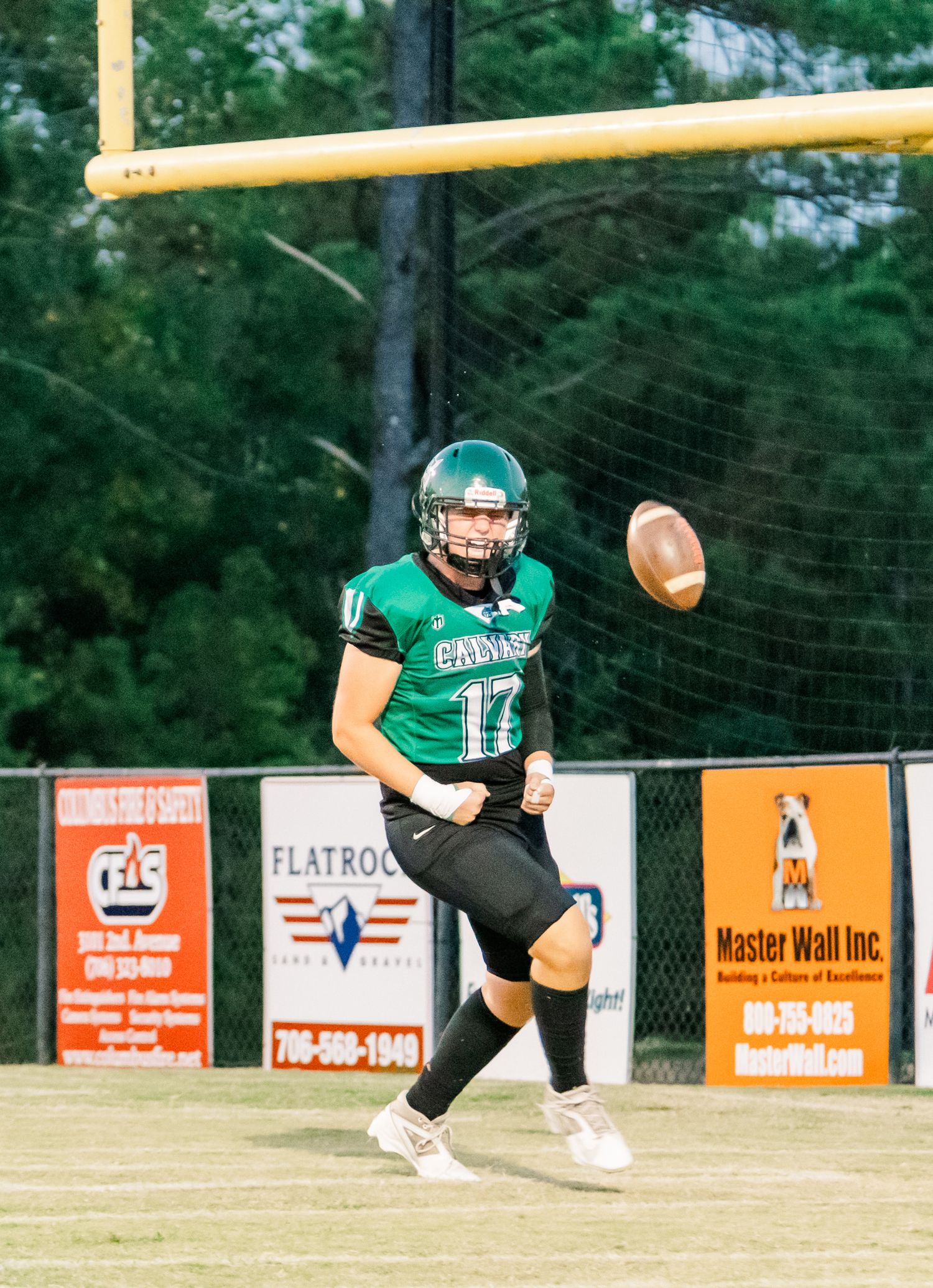 Football player #17 in green uniform kicks ball on field with yellow goalpost and sponsor banners visible.