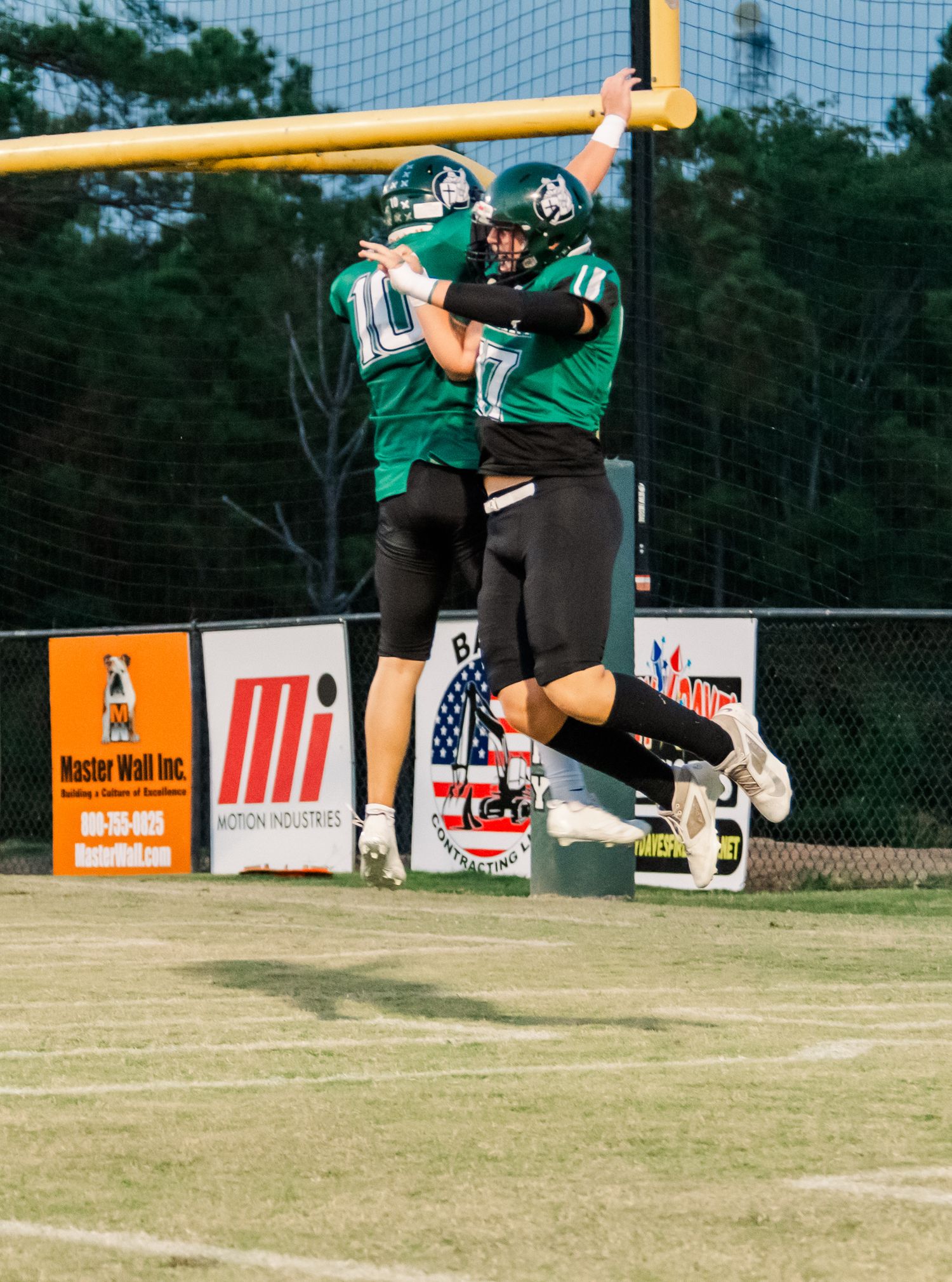 Two football players in green uniforms celebrate with a chest bump on the field during a game.