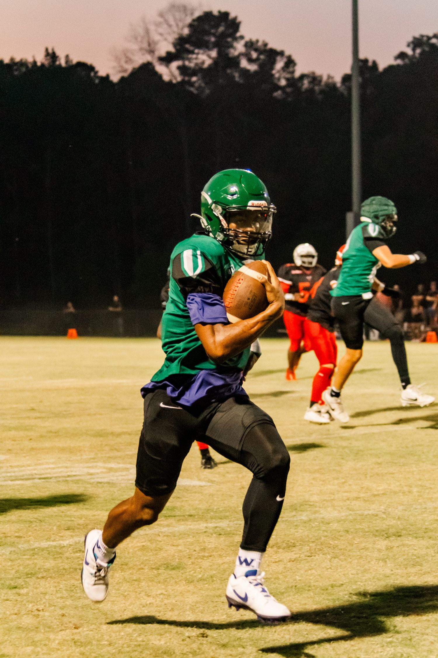 Football player in green uniform carrying ball during night game on field.