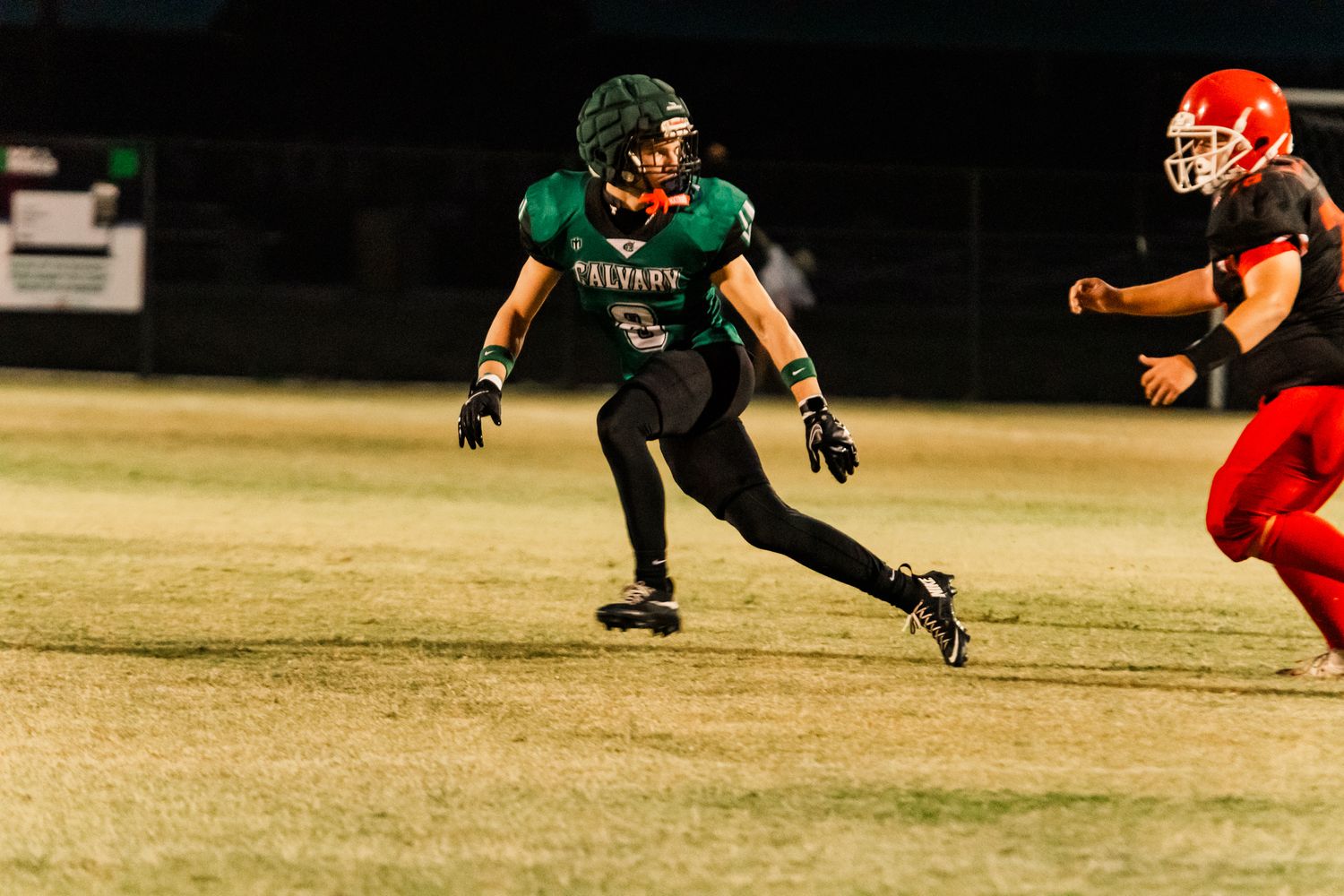 Football player in green Solvang jersey sprints on field during night game against red-uniformed opponent.