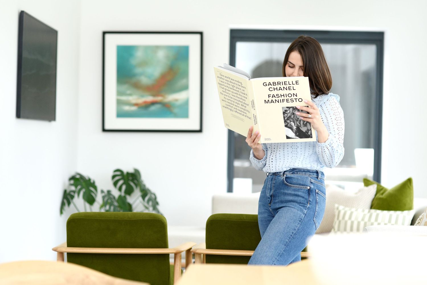 Someone reads a book while standing in a modern living room with green velvet chairs and wall art.  Bearwood House during a brand photoshoot