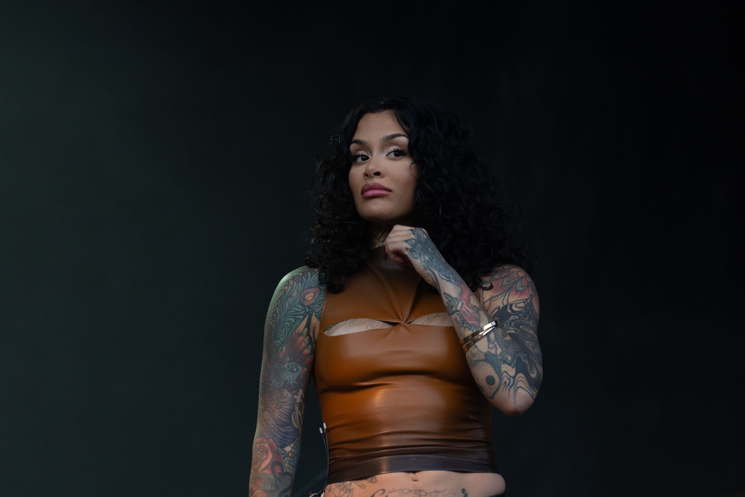 A figure in black lingerie poses against a dark background showing off tattoos and curves.