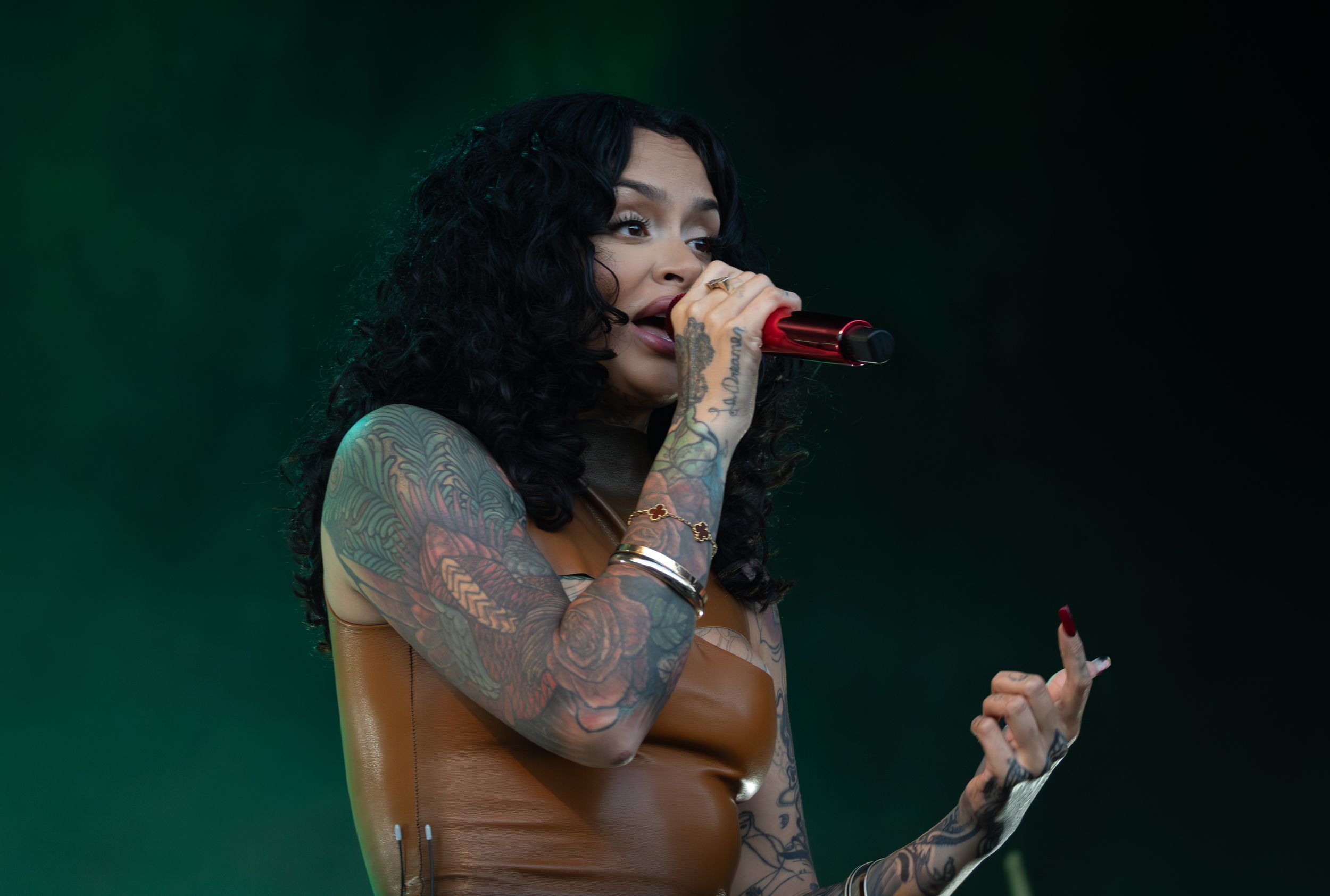 A performer in a black outfit sings passionately on stage with a dark green backdrop during a live concert performance.