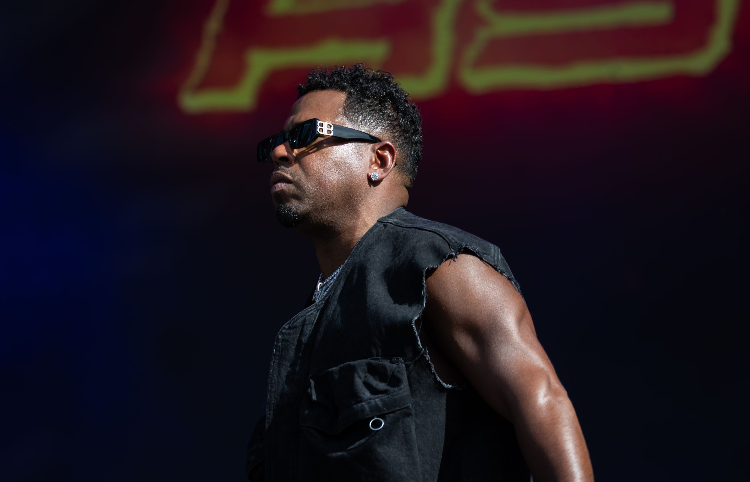 A muscular performer in a black tank top strikes dynamic poses during an energetic stage performance.