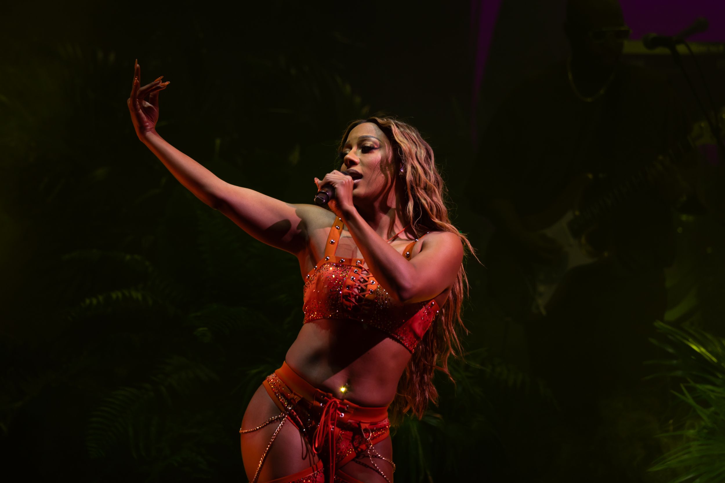 Dancer in flowing red dress performs expressive movement against dark background in dramatic lighting.