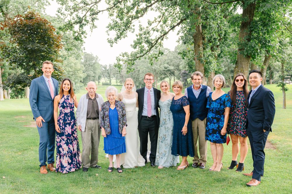 Family group photo outdoors with wedding party in formal attire.