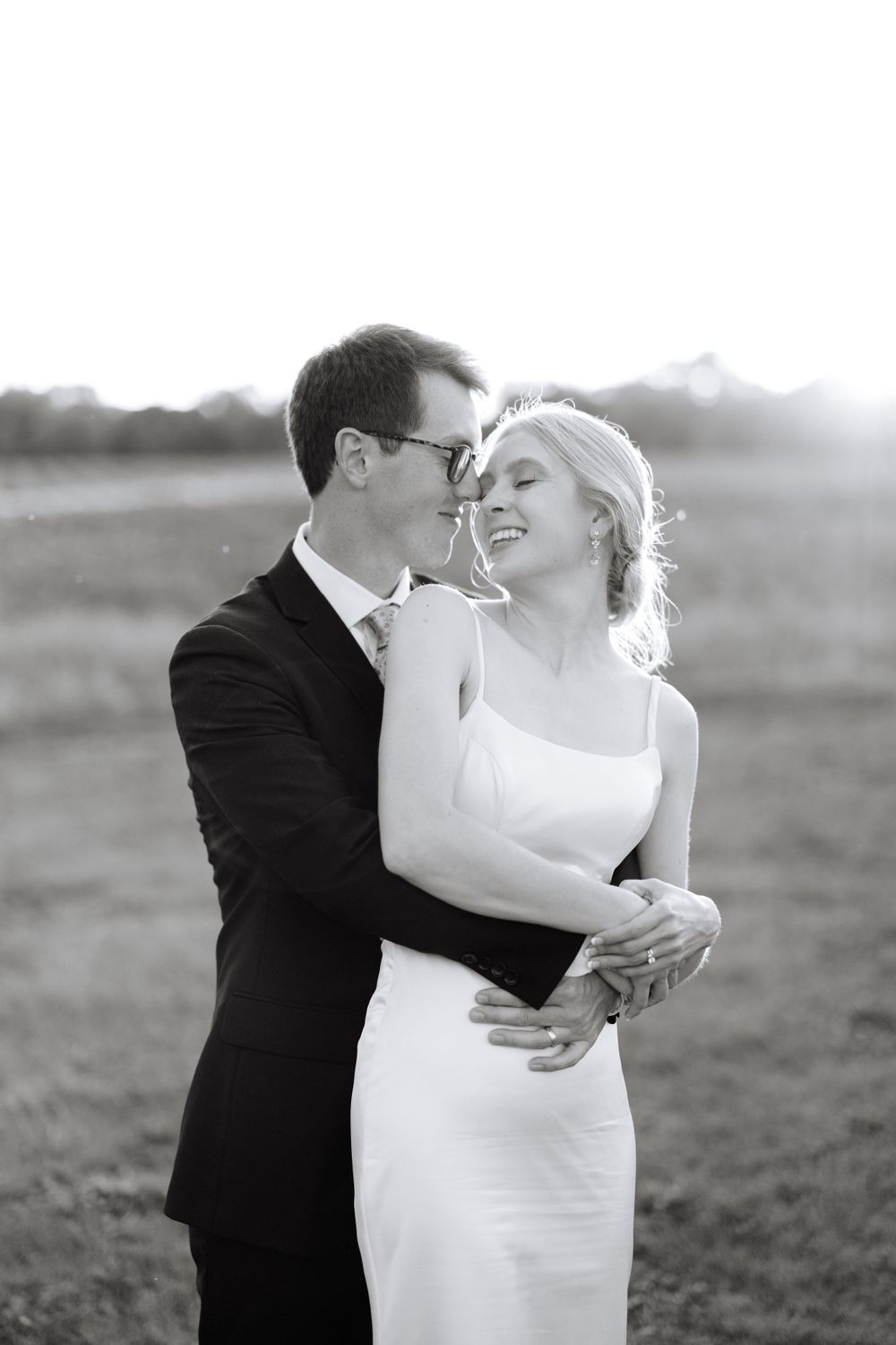 A tender black and white portrait of a bride and groom embracing in an outdoor field.