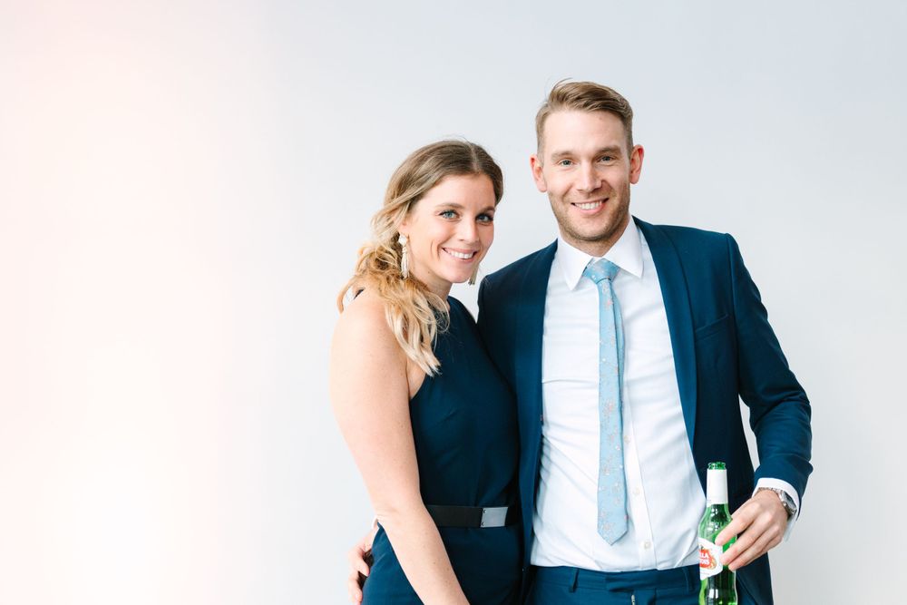 Couple in formal attire posing against white background with drinks.