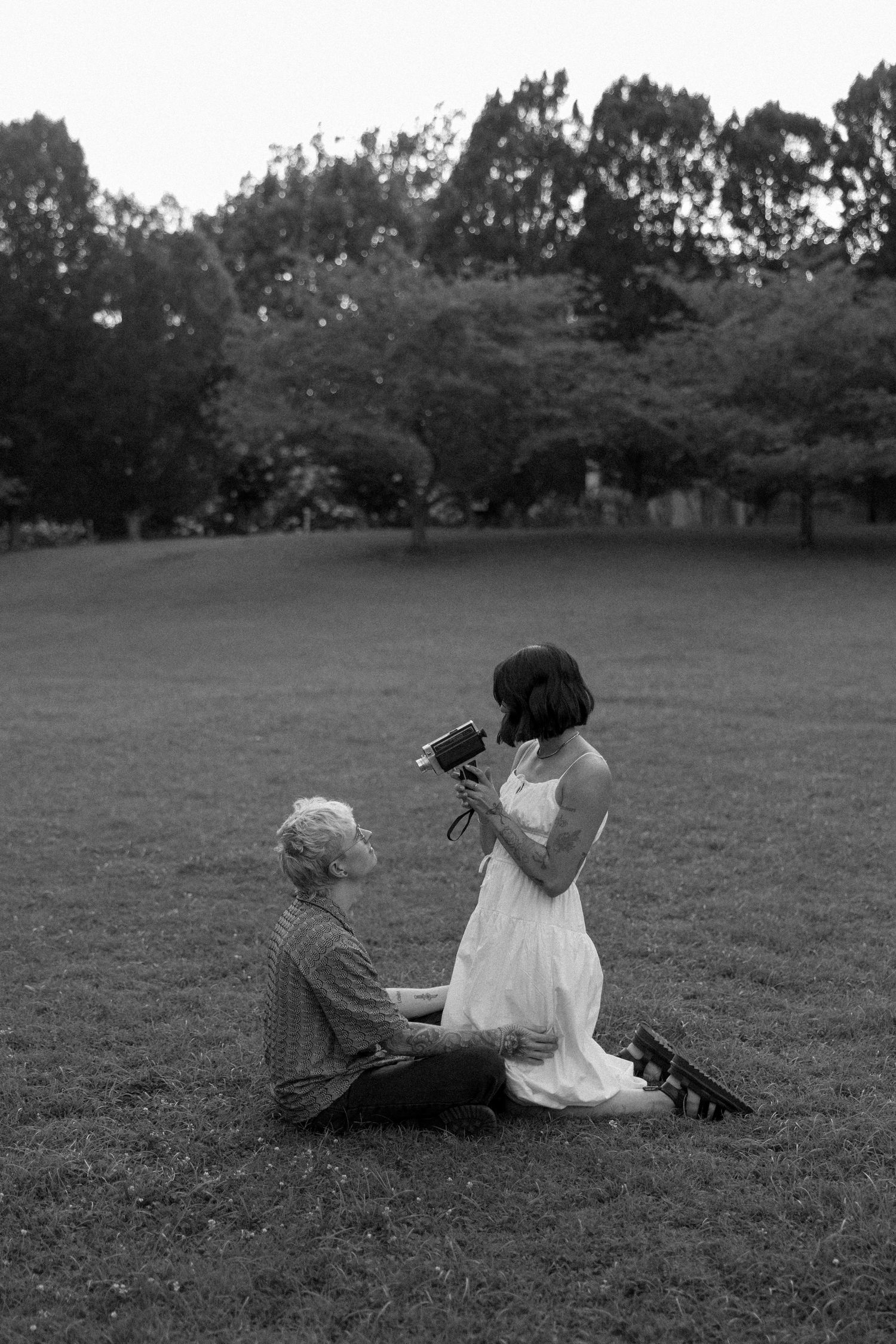 A romantic black and white photo of two people sitting on a grassy field while one examines something in their hands.