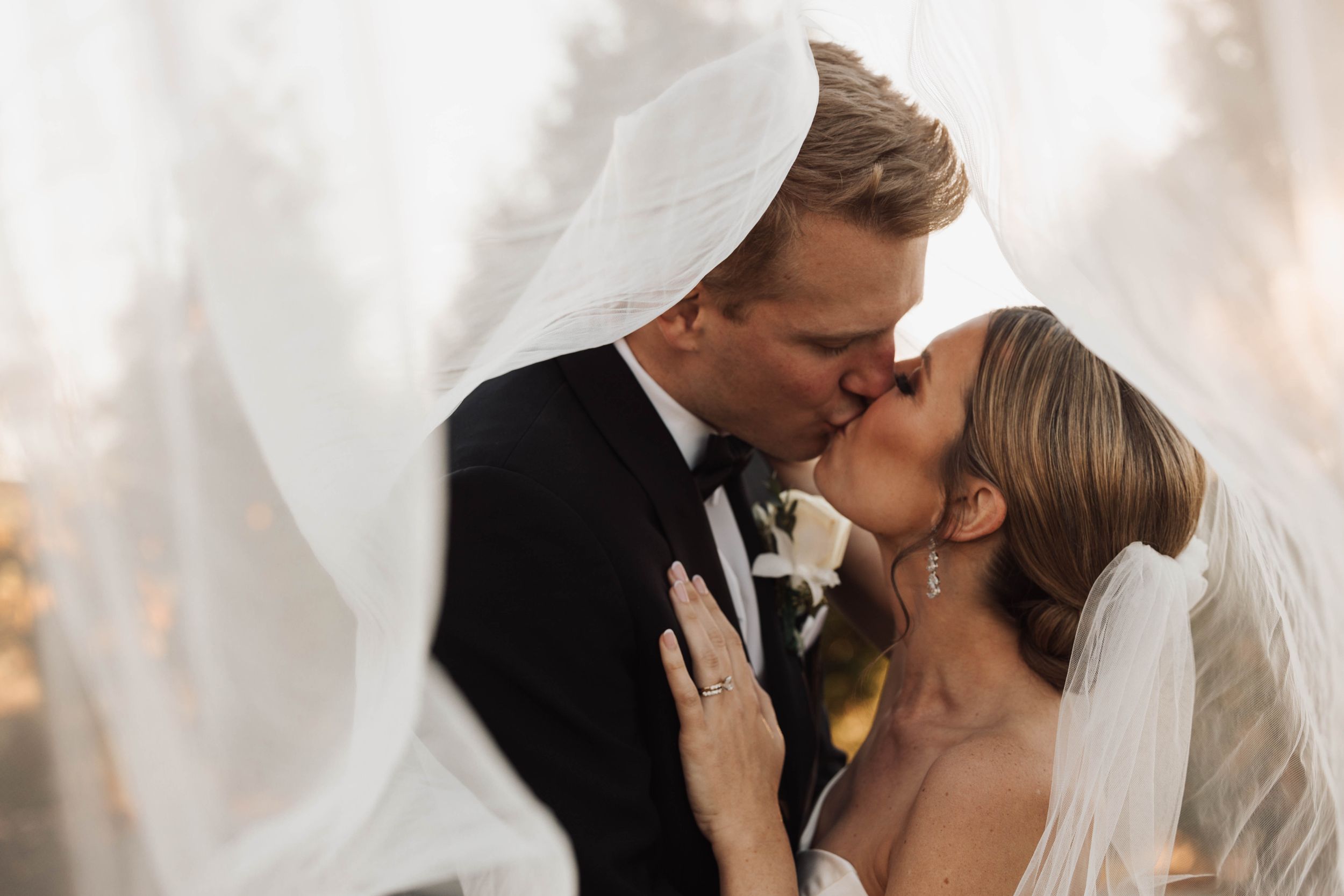 Bride and groom kissing softly beneath flowing wedding veil