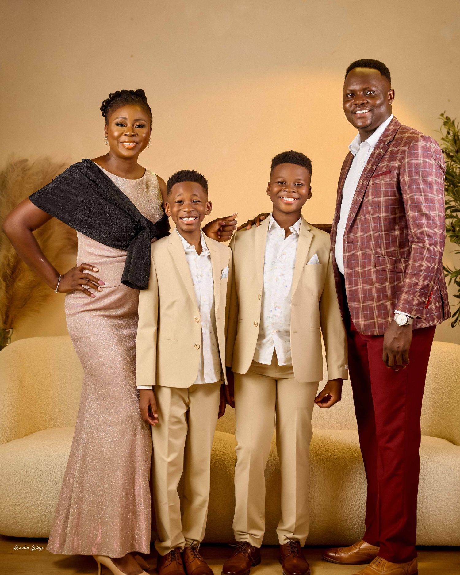 A family of four poses for a formal portrait wearing coordinated evening attire against a warm-toned backdrop.