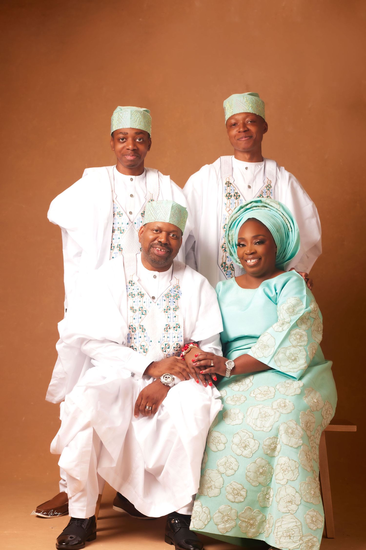 Traditional Nigerian family portrait in matching white and mint green formal attire against brown background.