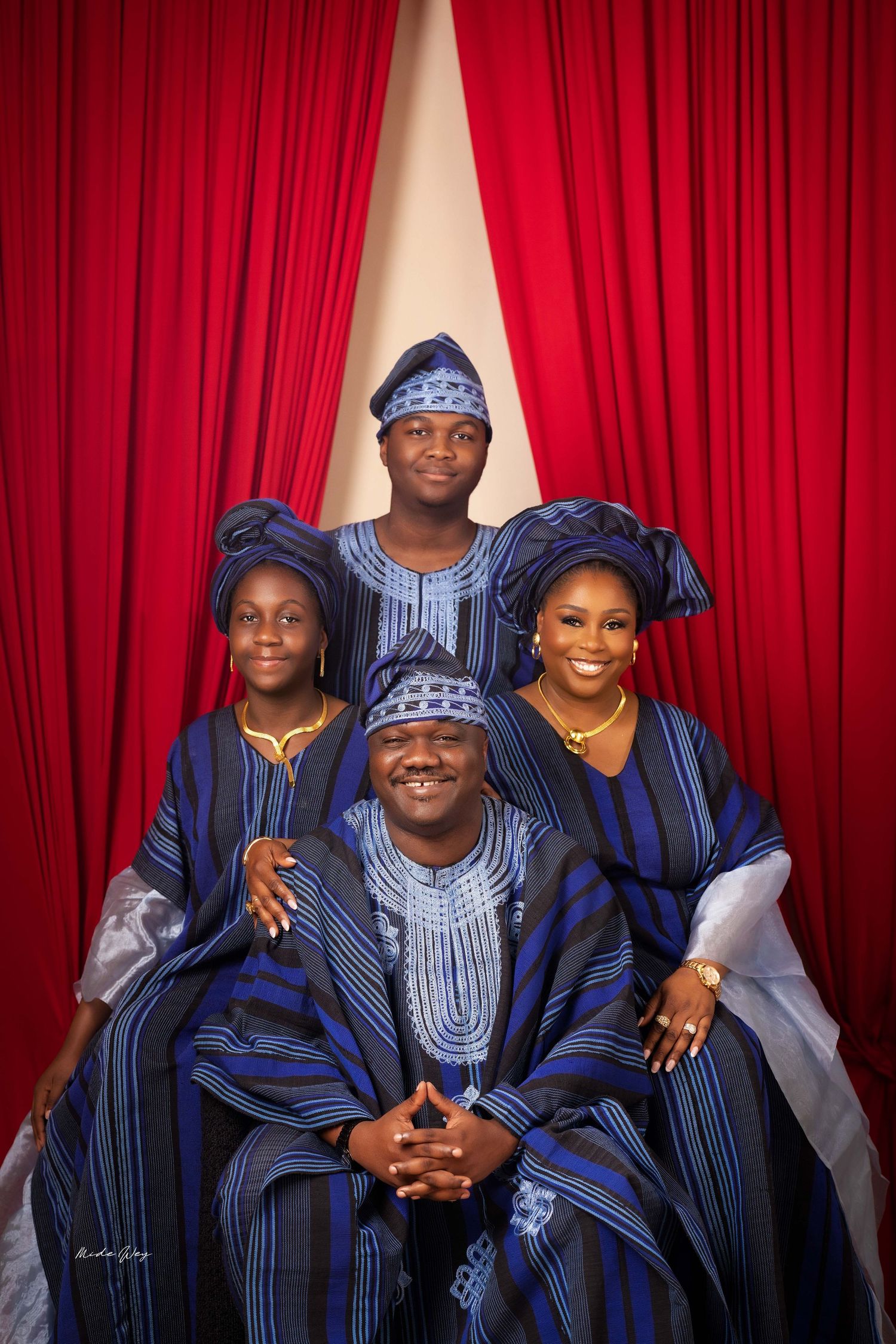 A group wearing traditional African attire poses together against a red curtain backdrop.