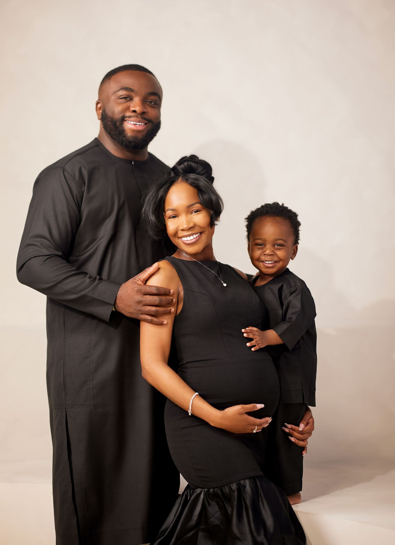 A family wearing matching black outfits poses together during a maternity photo shoot in a studio setting.